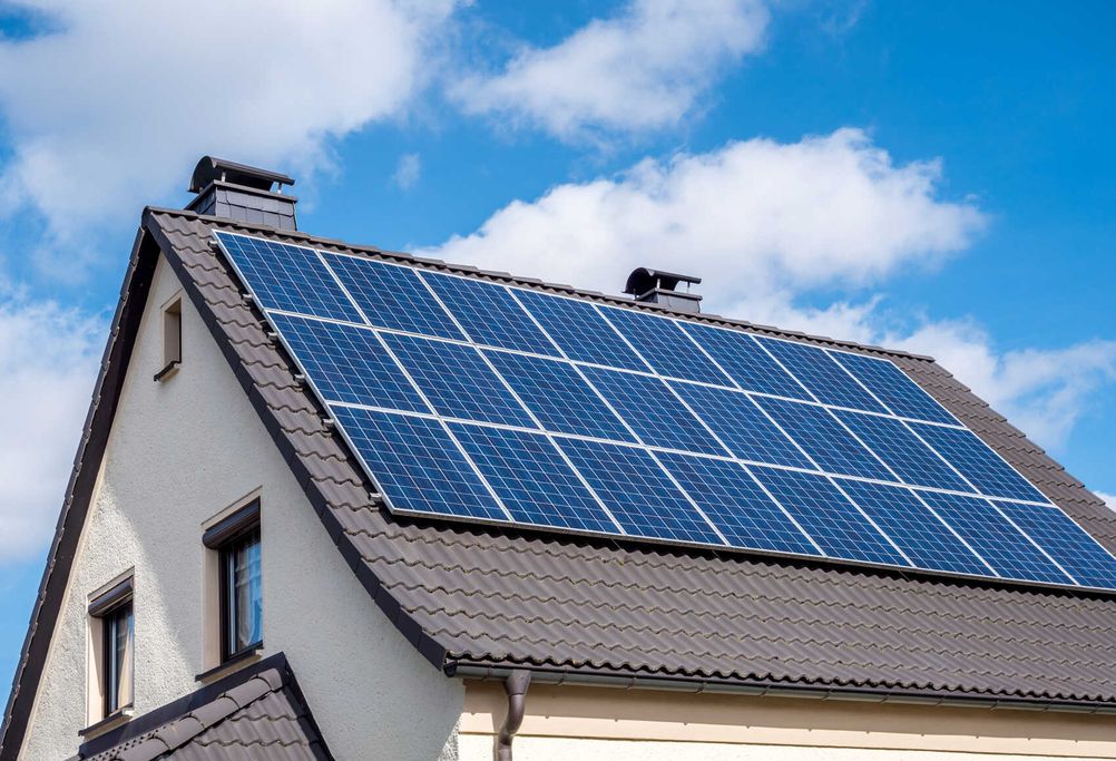 Auf dem grauen Dach eines weißen Hauses sind Solarmodule installiert