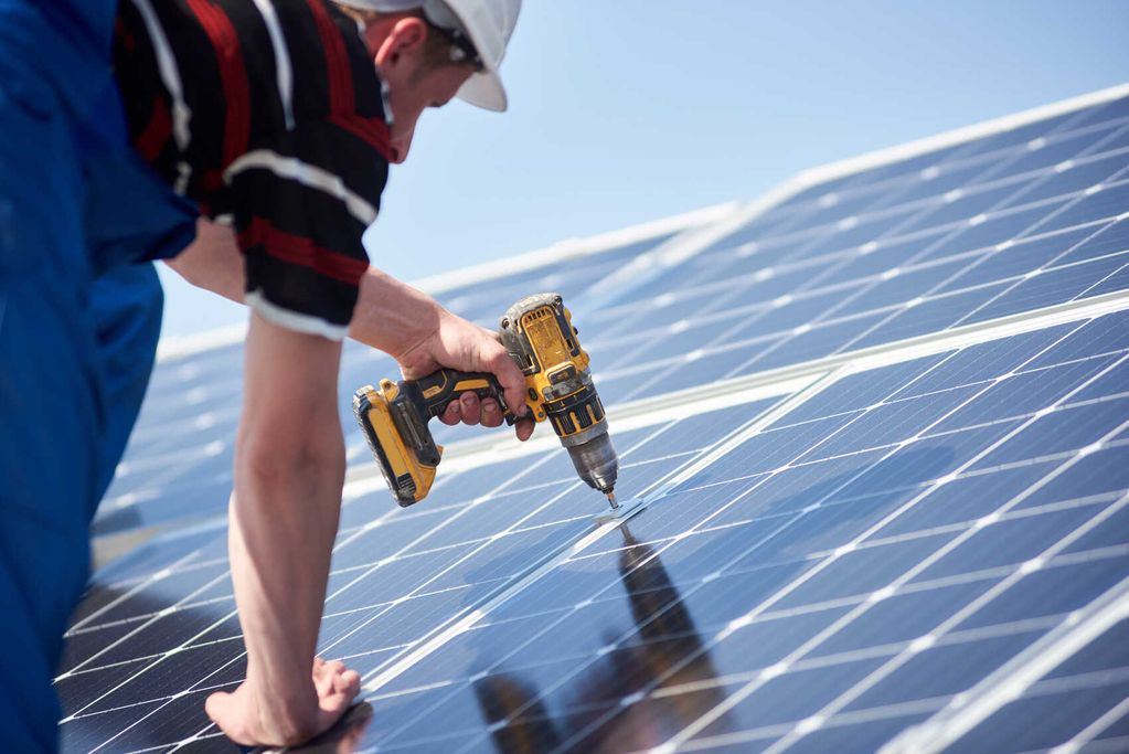 Ein Mann installiert Solarpanele mit einem Bohrer